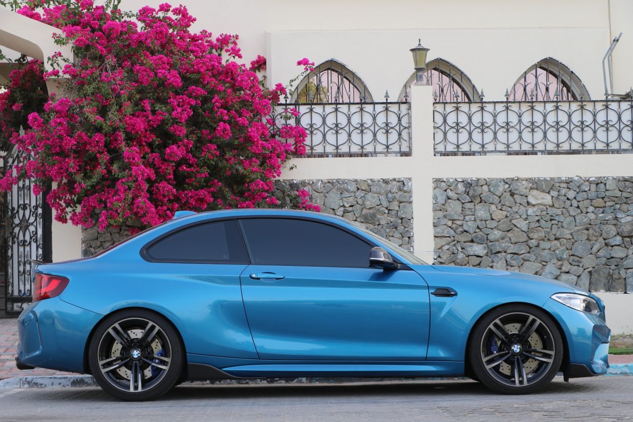 Blue sports car parked in front of flowering bougainvillea.